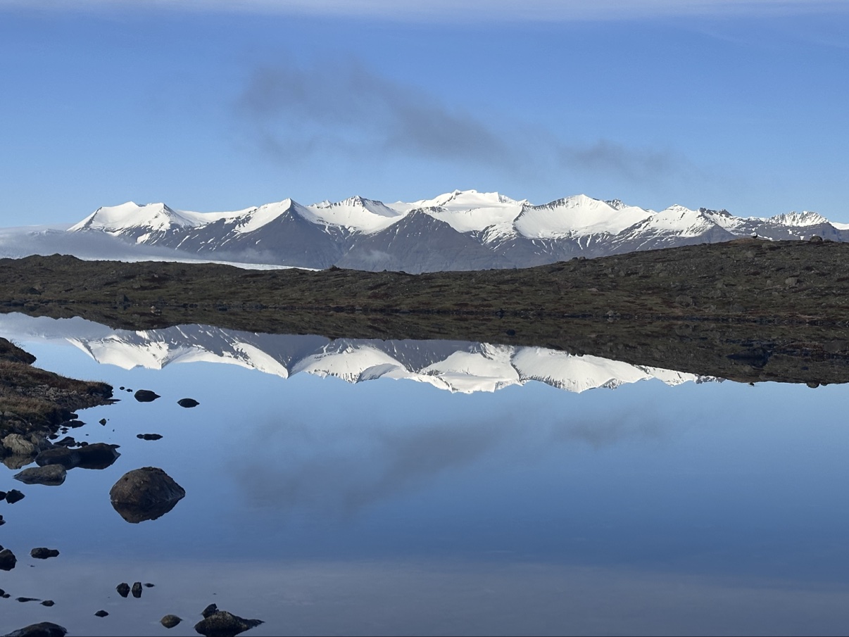 Snowy mountains reflected in a calm lake under a blue sky